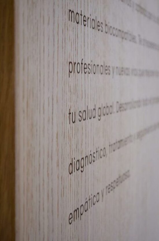Imagen detalle en vertical de la pieza de madera en la que se ha grabado un texto sobre la clínica Biodontology como parte de su diseño de interior llevado a cabo por Ideade Creativos.